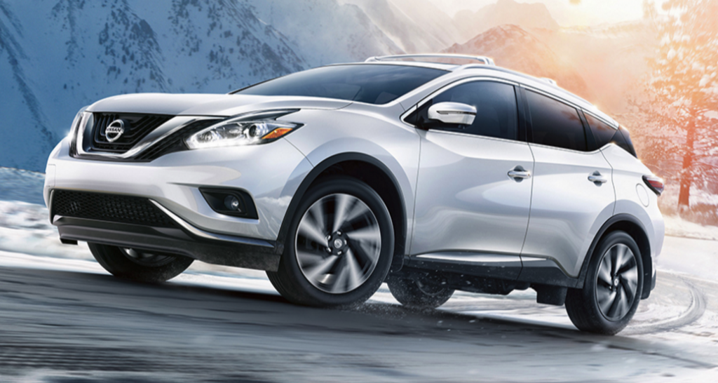 A white 2017 Nissan Murano driving down a snowy street with mountains in the background.