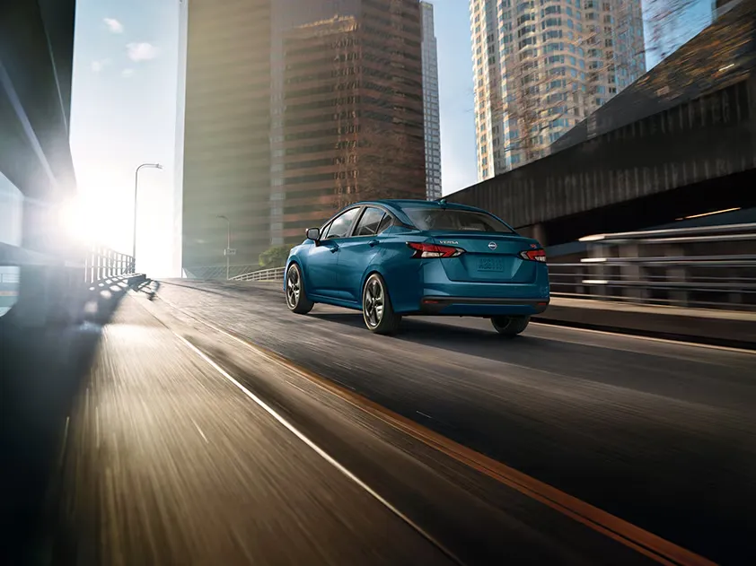 2025 Nissan Versa Sedan Driving in Urban Setting Blue 2025 Nissan Versa sedan driving through city highway