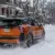 Orange and black 2026 Nissan Kicks SR crossover driving through snow with illuminated rear lights