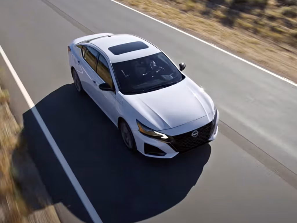 White Nissan Altima Driving on Paved Road White Nissan sedan traveling along a paved highway