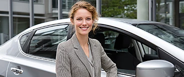 Smiling woman standing next to car at dealership