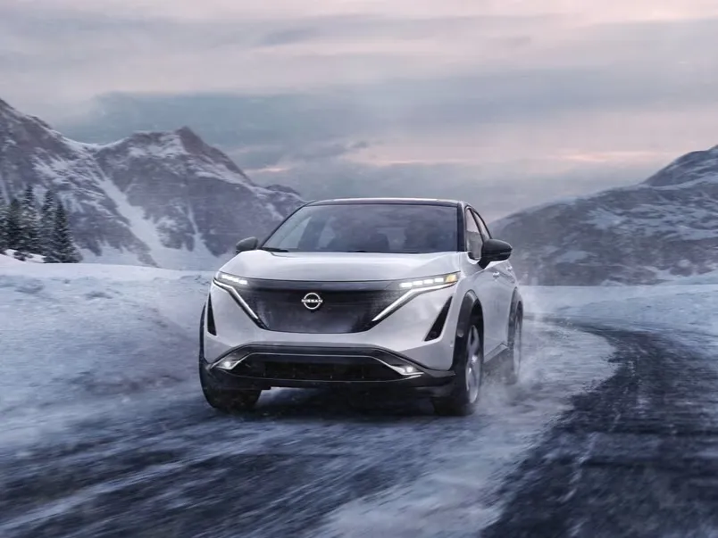 Silver Nissan Ariya on Snow Covered Mountain Road Silver Nissan Ariya driving on snow-covered road with mountains in background