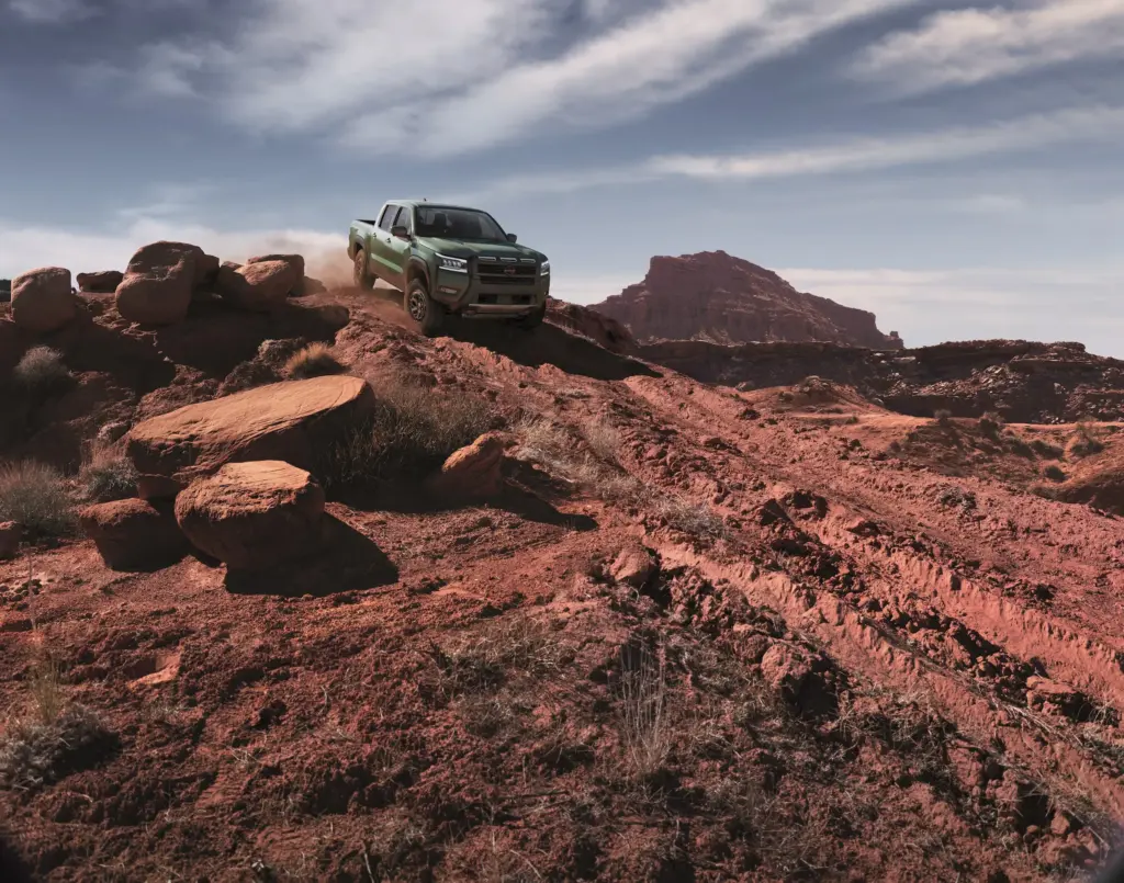 Green Nissan Frontier Driving Off Road on Rocks Green Nissan Frontier driving over rocky desert terrain