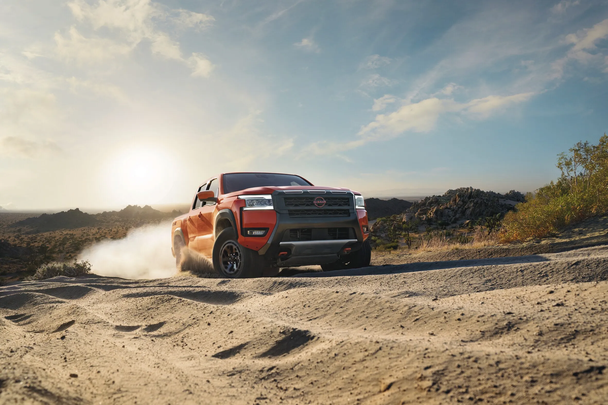 Red Nissan Frontier Driving Off Road in Desert Red Nissan Frontier driving on sandy desert terrain with dust behind