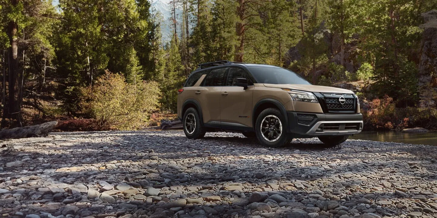 Tan Nissan Pathfinder SUV parked on a rocky riverbed surrounded by trees
