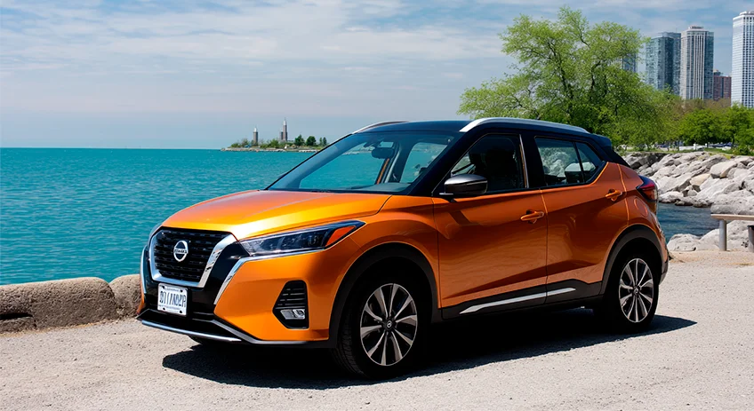 Orange Nissan Kicks Parked Near Lakefront With City Skyline Orange Nissan Kicks parked beside a lake with trees and city buildings in the distance