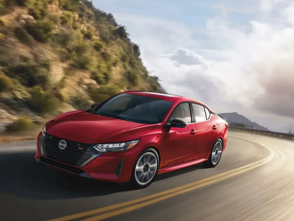 Red Nissan Sedan Driving on Mountain Road Red Nissan sedan driving on winding mountain road