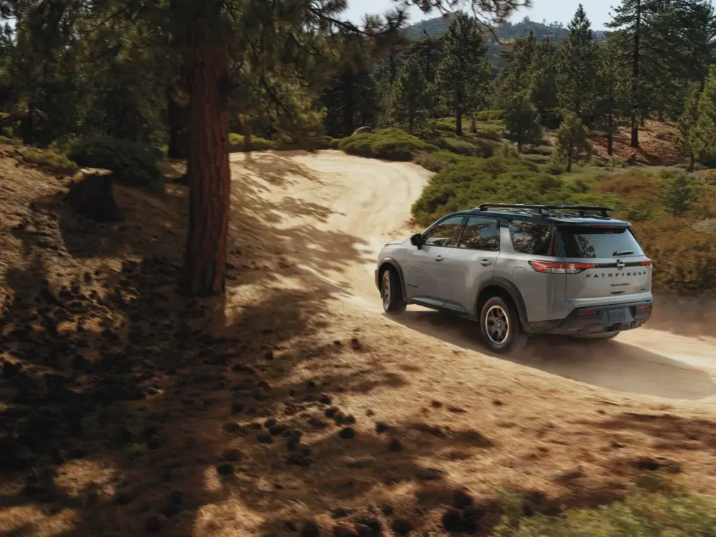 Silver SUV Driving on Winding Dirt Road in Forest Silver SUV driving on a winding dirt road through a forested area
