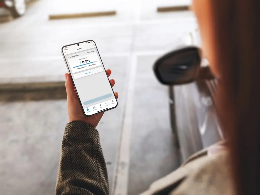 MyNISSAN App Showing Battery Charge Status Hand holding smartphone displaying electric vehicle battery charge level near parked car