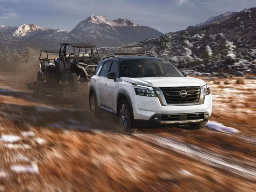White SUV Towing Off-Road Vehicle on Mountain Trail White SUV towing an off-road vehicle on a dirt trail with mountains in the background